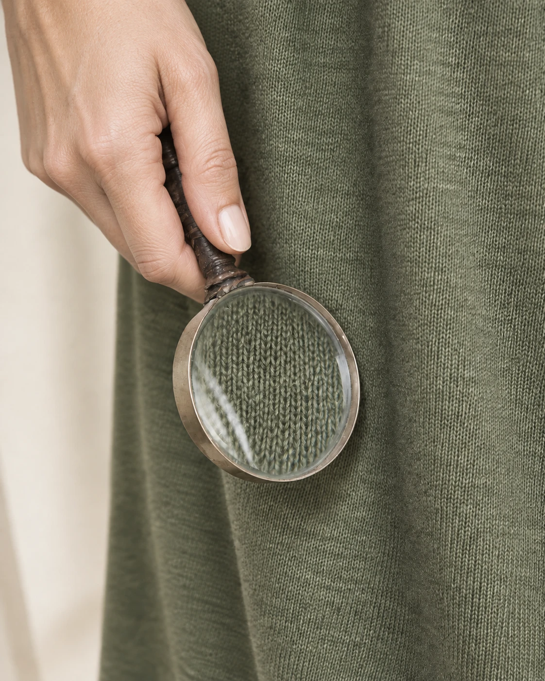 A hand holding a loupe over olive jersey